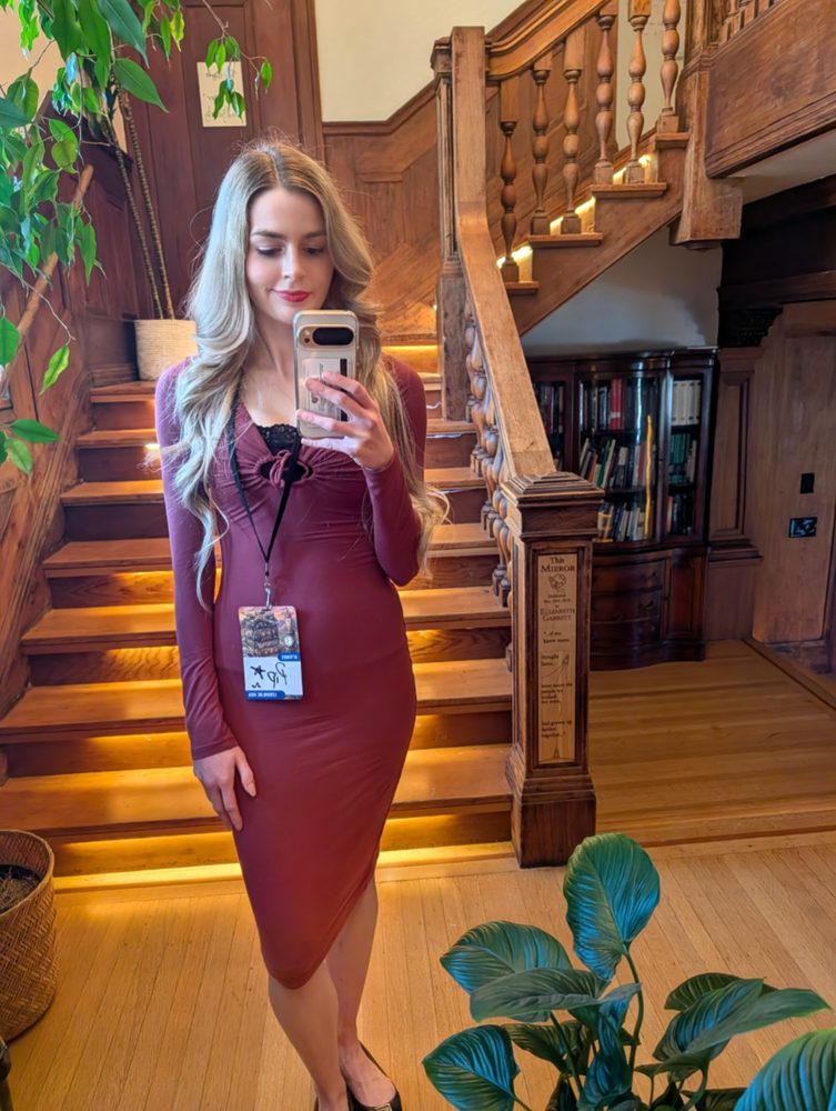 Full-length mirror photo of Pip in a burgundy dress at the foot of a wooden staircase
